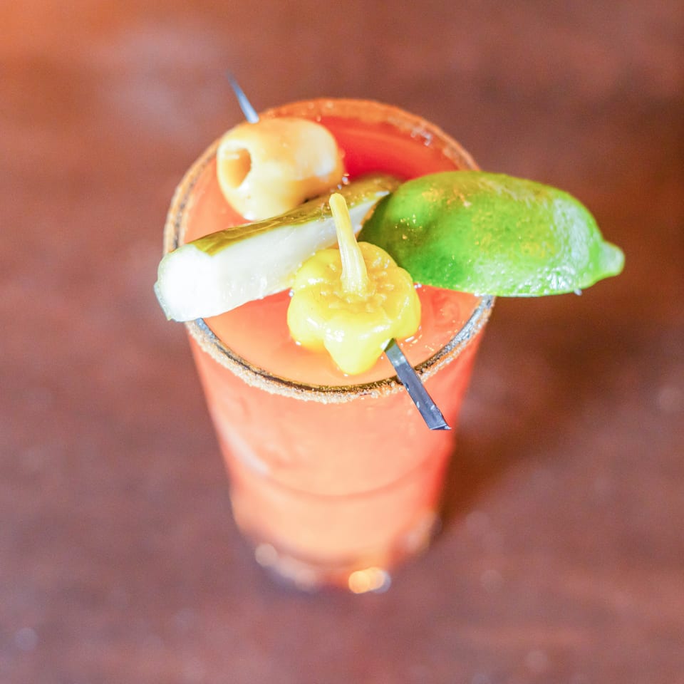 Colorful cocktail garnished with lime, cucumber, pineapple, and fruit, served in a glass with a sugared rim.