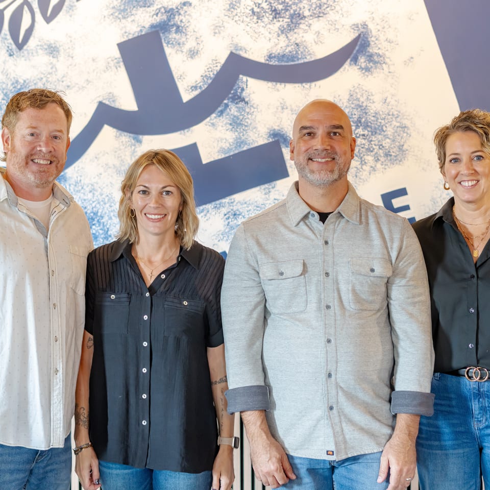 Four smiling restaurant team members pose together in front of a large blue-and-white branded wall.