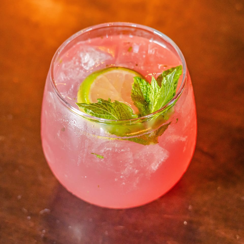 Pink iced cocktail garnished with a lime slice and fresh mint on a warmly lit wooden table.