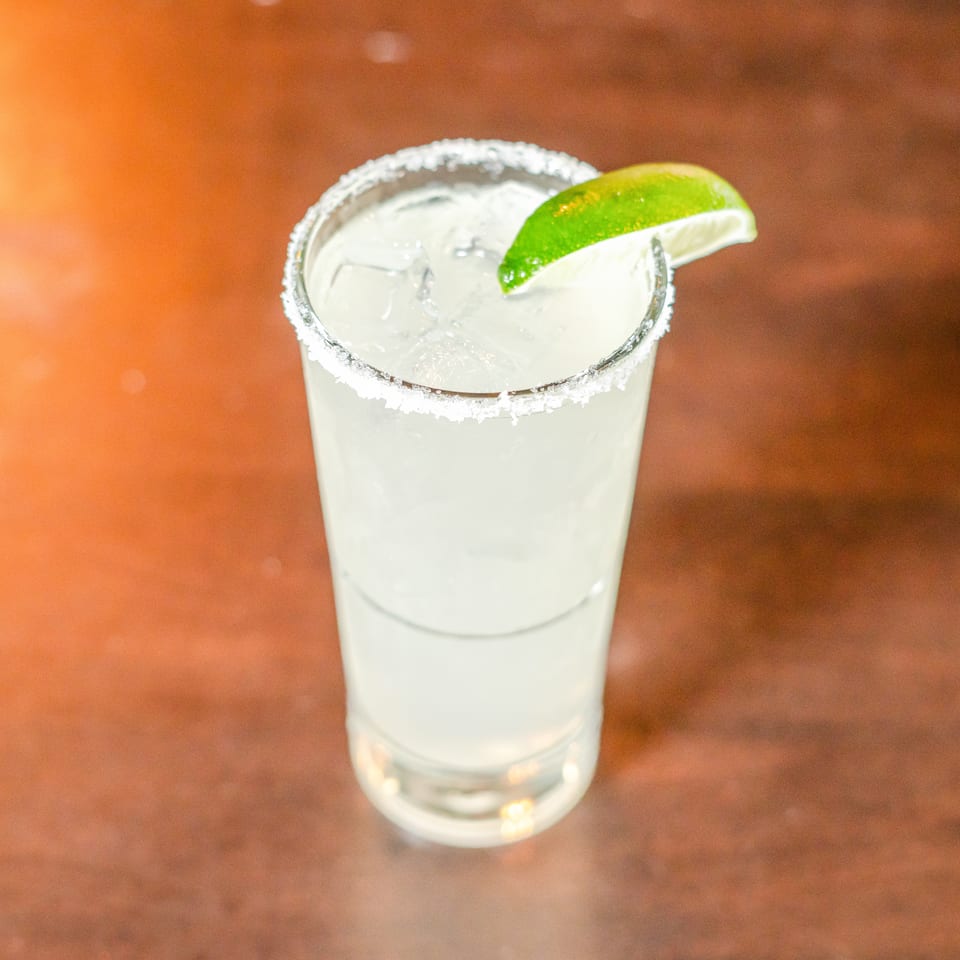 Margarita with a salt-rimmed glass, ice, and lime wedge on a warmly lit wooden table.