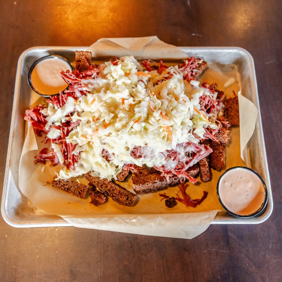 Loaded tray of toasted bread topped with shredded meat, creamy coleslaw, and two dipping sauces.