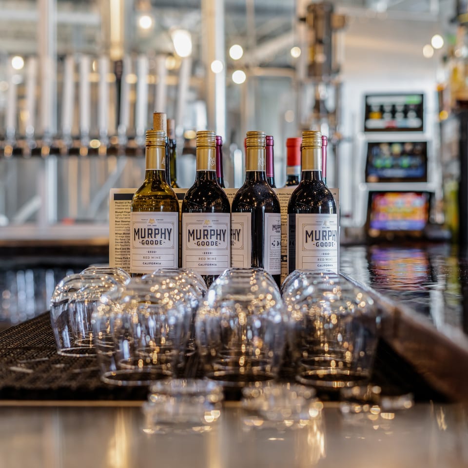 Murphy-Goode red and white wine bottles displayed on a polished restaurant bar with rows of glasses and blurred interior lights.