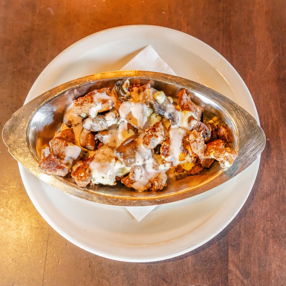 Loaded oval serving dish of grilled meat, mushrooms, and vegetables covered in creamy sauce on a white plate.