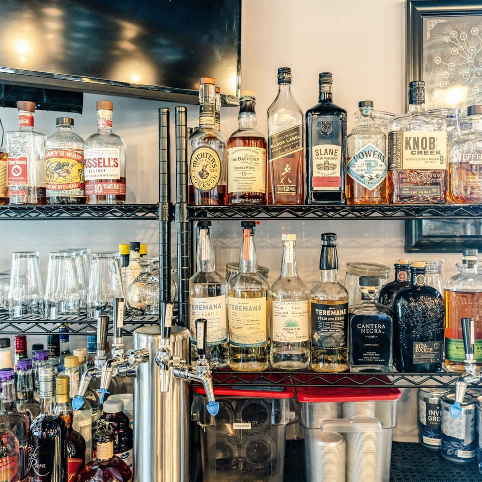 Shelves behind a bar display assorted whiskey, tequila, liqueurs, bottles, glassware, and beer taps.