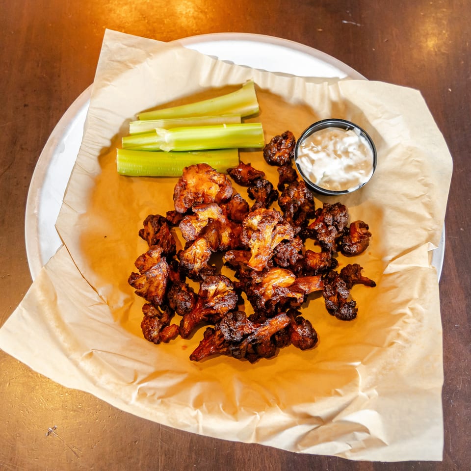 Crispy chicken wings served with celery sticks and creamy dipping sauce on a paper-lined plate.