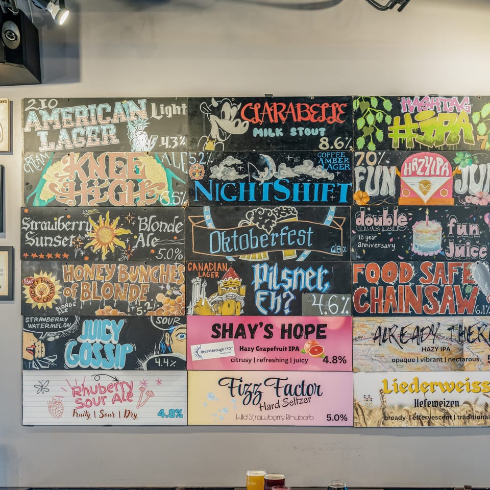 Colorful brewery taproom wall displays hand-painted beer boards, awards, and illustrated craft beer names and styles.