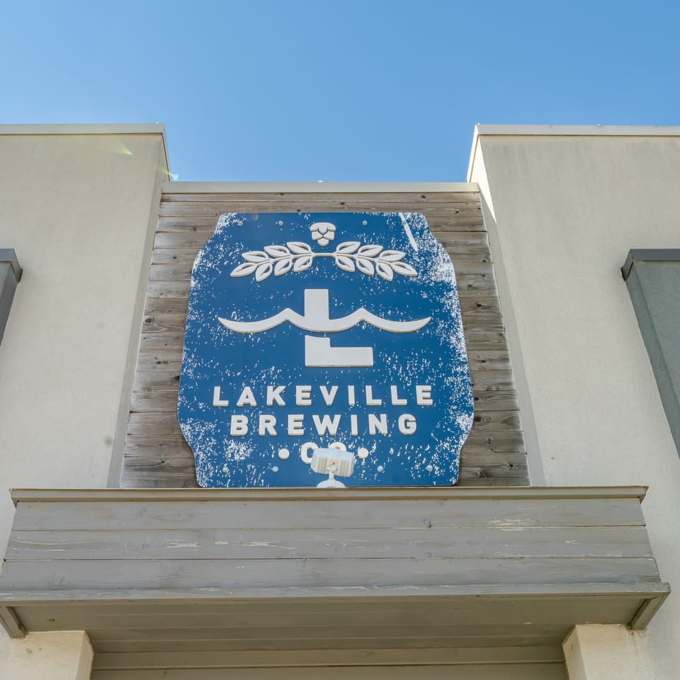 Lakeville Brewing Company sign mounted on a rustic wooden facade beneath a clear blue sky.